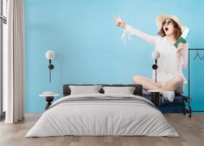 Young asian girl holding plane ticket and phone sitting on suitcase Wall mural