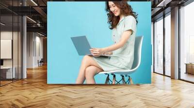 Young Asian girl sitting on a chair using a laptop with a happy expression Wall mural