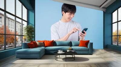 Young Asian man using smartphone on blue background Wall mural