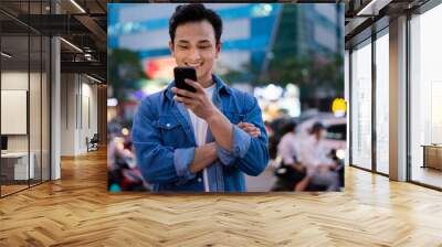 Young Asian man using smartphone on the street at night Wall mural