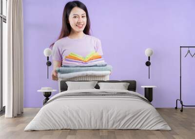 Young Asian woman holding a stack of clothes on purple background Wall mural