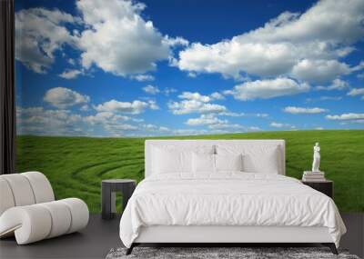 A crop circle in a green field, with a cow grazing at its center, beneath a vivid blue sky filled with fluffy white clouds Wall mural