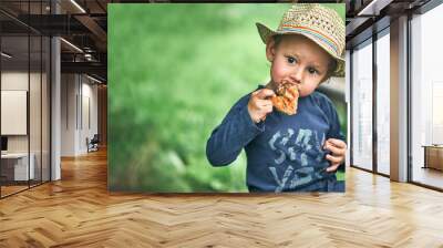 Boy in straw hat eats grilled chicken wing in green yard Wall mural