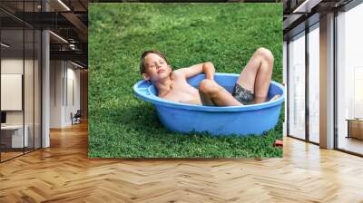 Relaxed boy lies in plastic basin on green lawn grass Wall mural