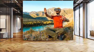 Successful young man, using virtual reality goggles to tour in mountains, on vacation in summer Wall mural