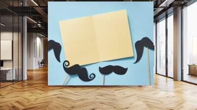 Mockup black mustaches on blue paper background top view. Happy fathers day greeting card with yellow sheet of paper and place for text. Hipsters objects flat lay Wall mural