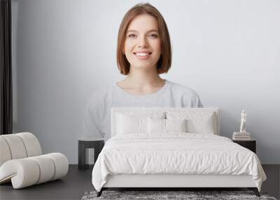 beautiful woman expresses happy emotions, has broad pleasant smile, wears white longsleeve and feels satisfied. Isolated over white background Wall mural