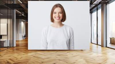 beautiful woman expresses happy emotions, has broad pleasant smile, wears white longsleeve and feels satisfied. Isolated over white background Wall mural