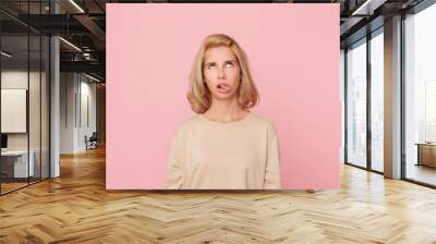 Bored to death! Young blonde female, feels drearily and looks above, shows her tongue with disgust. Isolated over pink background. Wall mural