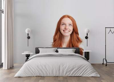 Closeup of cheerful beautiful young woman with long wavy red hair and freckles wears t shirt feels happy and looks up isolated over white background Wall mural