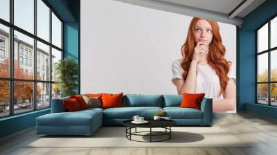 Closeup of cute thoughtful redhead young woman with long wavy hair and freckles wears stylish t shirt thibnking and planning her working day isolated over white background Wall mural