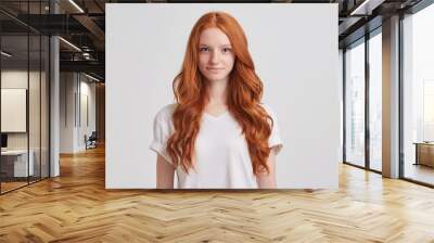 Closeup of happy attractive young woman with long wavy red hair and freckles wears stylish t shirt looks happy and smiling isolated over white background Wall mural