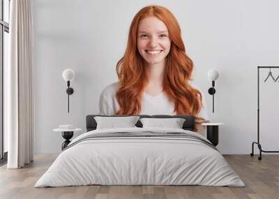 Closeup of happy pretty redhead young woman with long wavy hair and freckles wears stylish t shirt feels satisfied and looks confident isolated over white background Wall mural