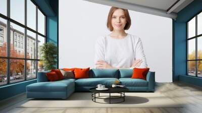 Closeup of happy pretty young woman in longsleeve standing with hands folded and looking directly in camera isolated over white wall Feeling confident Wall mural