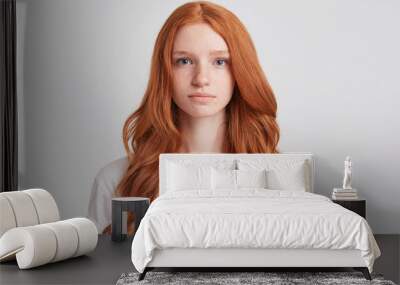 Closeup of serious beautiful redhead young woman with long wavy hair and freckles wears t shirt feels confident and looks directly in camera isolated over white background Wall mural