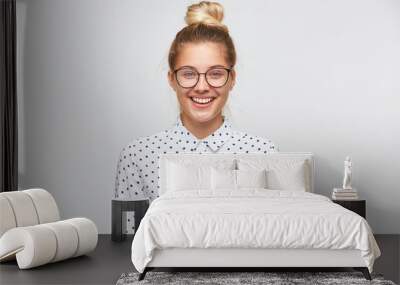 Closeup of smiling pretty young woman with bun wears polka dot shirt and glasses feels happy and confident isolated over white background Wall mural