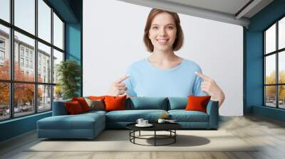 Happy confident young woman in blue t shirt smiling and pointing at herself with fingers on both hands isolated over white background Wall mural