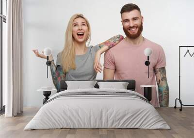 Horizontal shot of young attractive tattoed couple being in high spirit and smiling widely while posing over white background in grey and pink basic t-shirts Wall mural