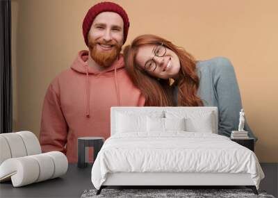 Indoor shot of cheerful redhead woman, keeps her hand on boyfriend shoulder, smiles and feels happy. family album image of Caucasian couple enjoy their partnership. Isolated over biege background Wall mural