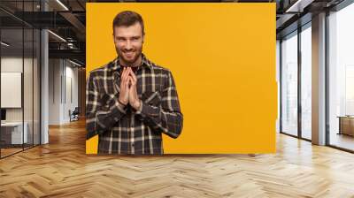 Mischievous arrogant young man in plaid shirt with beard rubbing hands and scheming an evil plan over yellow background Looking away to the side Wall mural