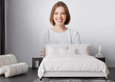 Portrait of cheerful attractive young woman in longsleeve standing with arms crossed and smiling isolated over white background Looks confident Wall mural