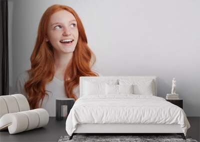 Portrait of cheerful attractive young woman with long red wavy hair wears t shirt feels happy and looks to the side isolated over white background Wall mural