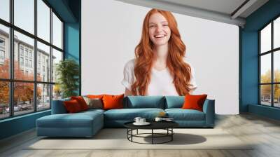 Portrait of cheerful cute redhead young woman with long wavy hair and freckles wears stylish t shirt looks relaxed and laughing isolated over white background Feels happy Wall mural