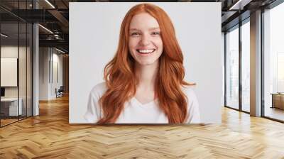 Portrait of cheerful pretty redhead young woman with long wavy hair and freckles wears t shirt feels joyful and laughing isolated over white background Looks directly in camera Wall mural