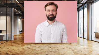 Portrait of young calm smiling handsome bearded man, wearing a white shirt. Looking at the camera isolated over pink background. Wall mural