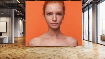 Studio photo of beautiful young readhead female with casual hairstyle standing over orange background without clothes, looking at camera with calm face Wall mural