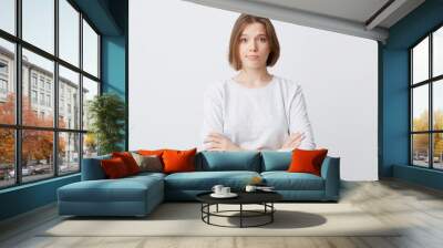 Unhappy dissatisfied young woman in longsleeve standing with hands folded and feels disappointed isolated over white background Wall mural