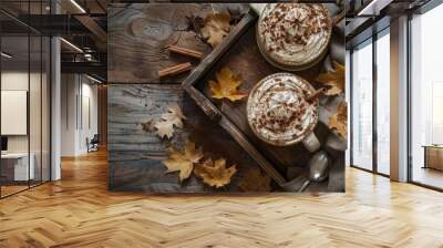 Cozy autumn scene with two mugs of hot chocolate topped with whipped cream and cinnamon on rustic wooden table surrounded by fall leaves. Wall mural