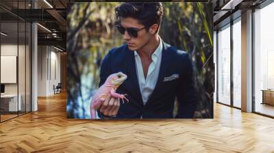 Attractive young man in suit holding pink lizard in swamp Wall mural