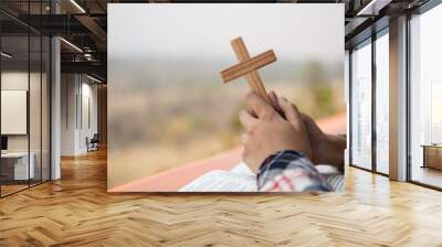 close up young hands holding wooden cross over holy bible and praying. christian concept Wall mural