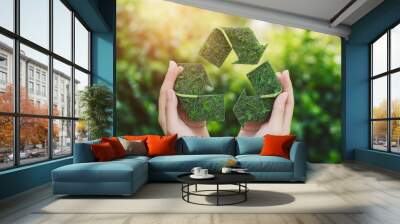 Hands holding a green recycling symbol made of leaves, symbolizing sustainability and environmental protection. Wall mural