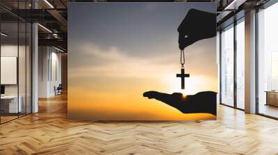 Silhouette of hand holding necklace crucifix background sunrise. Concept for Christian, Christianity, Catholic religion,  god. Wall mural