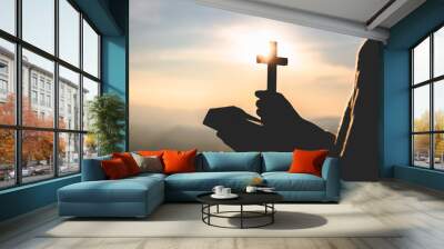 Silhouette of Young woman hands holding holy Bible and lift of christian cross, religion symbol in light and landscape over a sunrise, background, religious, faith concept Wall mural