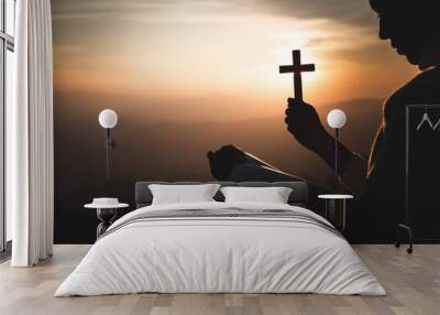 Silhouette of young woman hands holding holy Bible and lift of christian cross with light sunset background. Pray with the cross. christian concept Wall mural