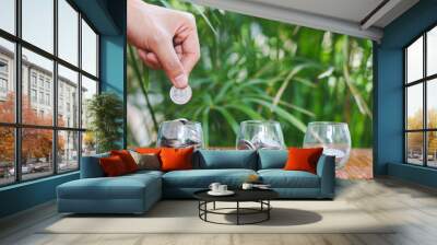 Woman's hand putting coin into glass of bottle for saving money, Saving money concept Wall mural