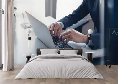 Business man working on laptop computer at modern office. Businessman in black suit working and typing on laptop keyboard, surfing the internet with digital tablet on office table Wall mural