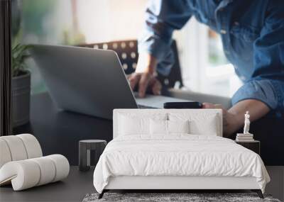 Close up of man using mobile smart phone and working on laptop computer on wooden table at home with blurred background Wall mural