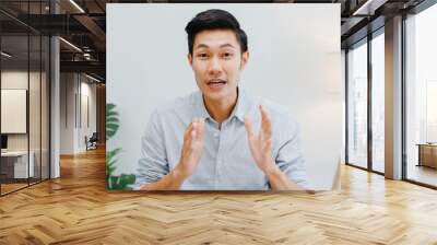 Asia businessman social distancing in new normal situation for virus prevention looking at camera presentation to colleague about plan in video call while work in office. Lifestyle after corona virus. Wall mural