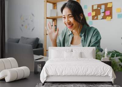 Asia businesswoman using laptop talk to colleagues about plan in video call while smart working from home at living room. Self-isolation, social distancing, quarantine for corona virus prevention. Wall mural