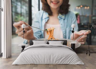 Beautiful happy Asian woman eating a plate of Italian seafood spaghetti at restaurant or cafe while smiling and looking at food. Wall mural