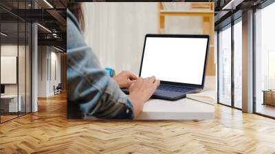 Creative young asia woman sitting at Her desk using laptop with mock up white screen in the cozy living room at modern home. Wall mural