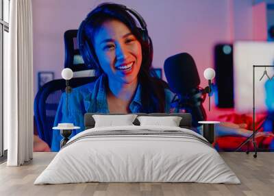 Happy asia girl blogger music influencer use smartphone broadcast recording wear headphone online live talk with listening audience in living room home studio at night. Content creator concept. Wall mural