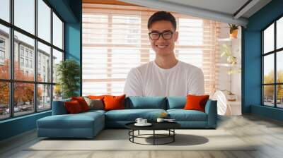 Happy young Asian male feeling happy smiling, arms crossed and looking to camera while relax in kitchen at home. Lifestyle man at home concept. Wall mural