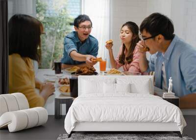 Happy young friends group having lunch at home. Asia family party eating pizza food and laughing enjoying meal while sitting at dining table together at house. Celebration holiday and togetherness. Wall mural