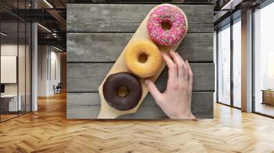 Glazed three donuts in a row on a wooden board background with blank space. Woman's hand reaches for a yellow handwriting, wants to taste Wall mural