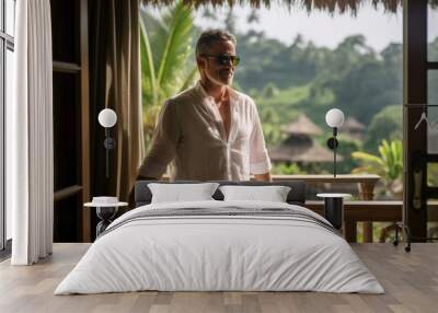 a successful middle-aged man of european appearance, dressed in white, enjoys a gorgeous view of the rice fields from the balcony of his villa. Wall mural